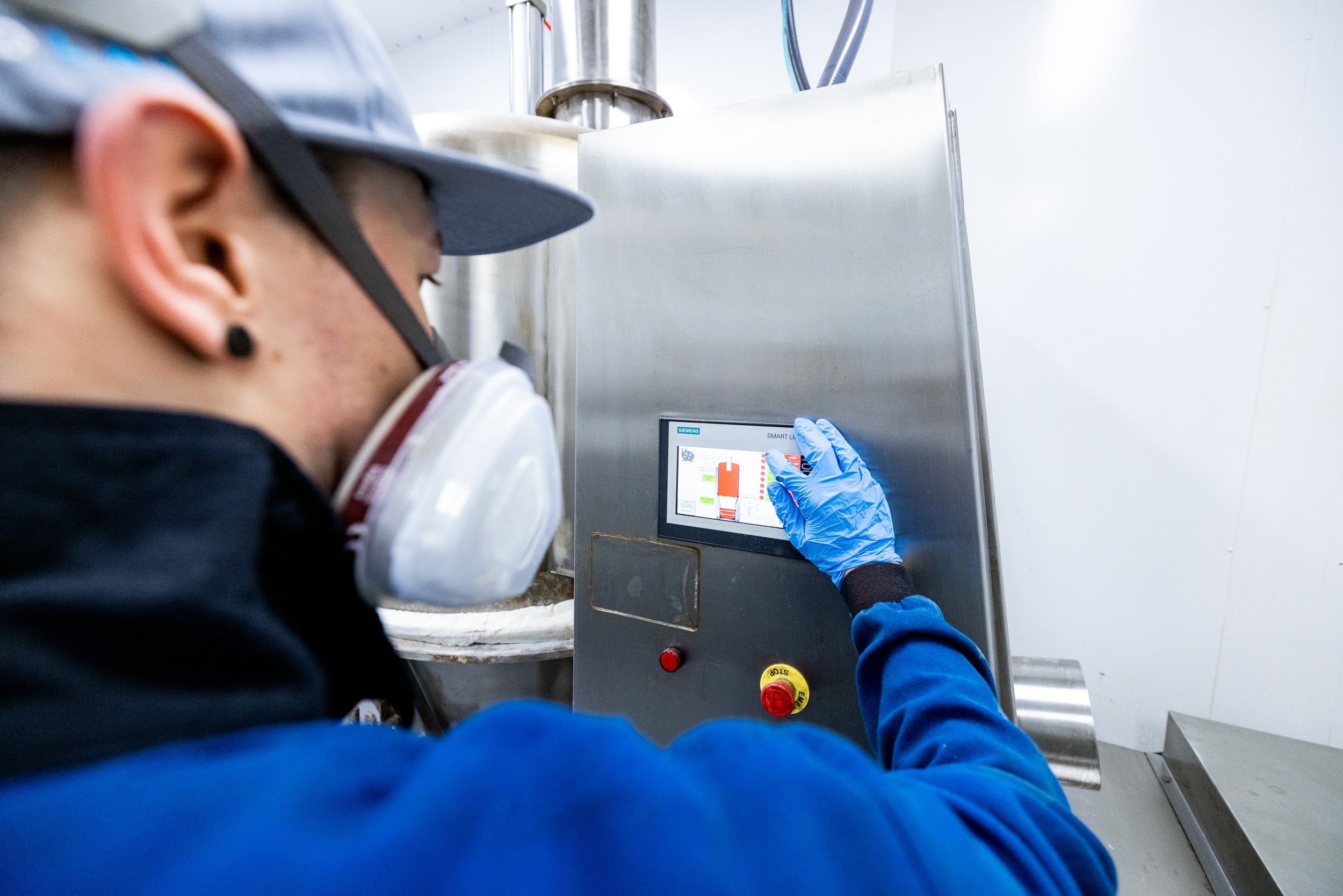 A man in a blue shirt and gloves operates a machine, focused on his task in a work environment.