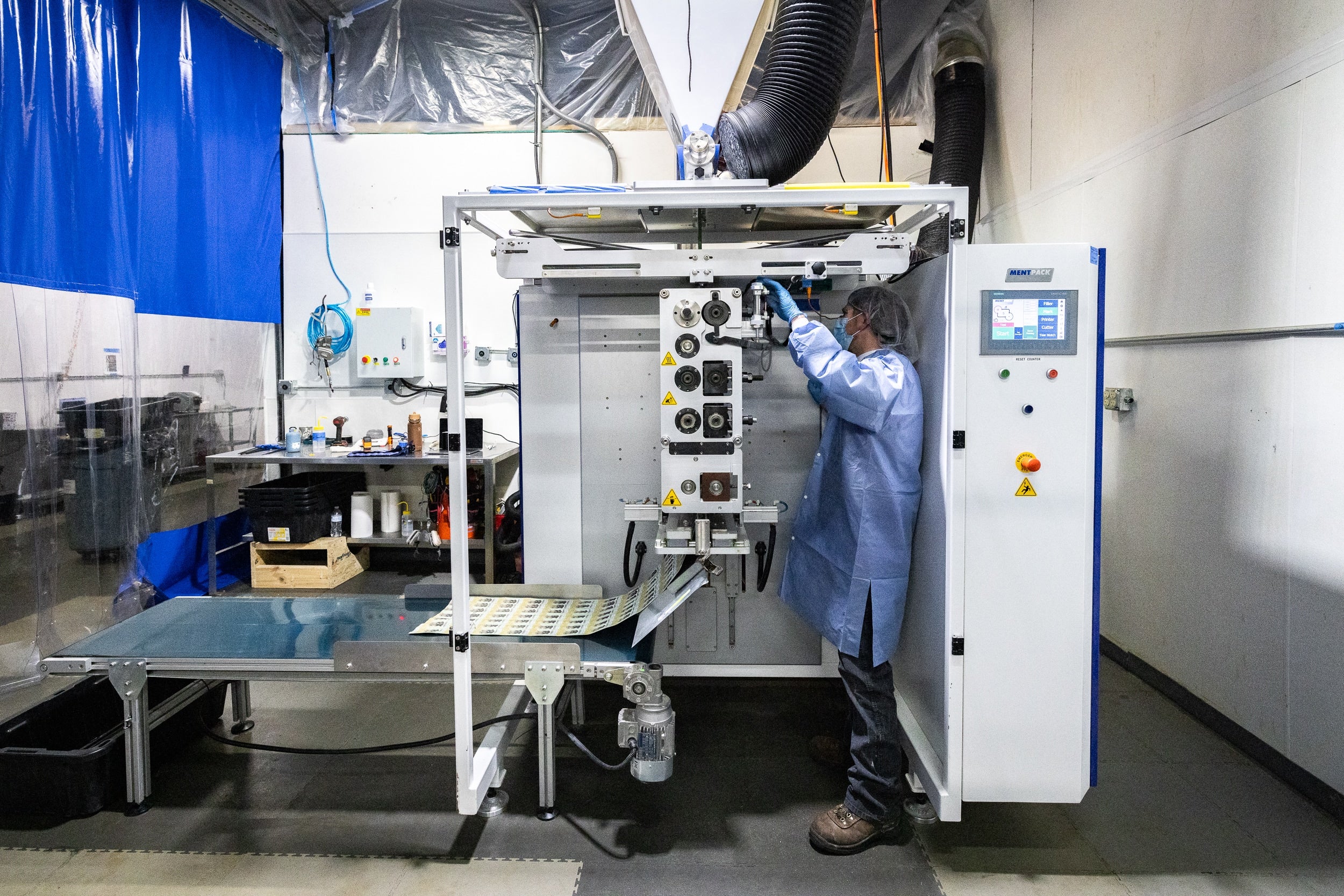 A man in a blue coat operates a machine, focused on his task in a workshop setting.