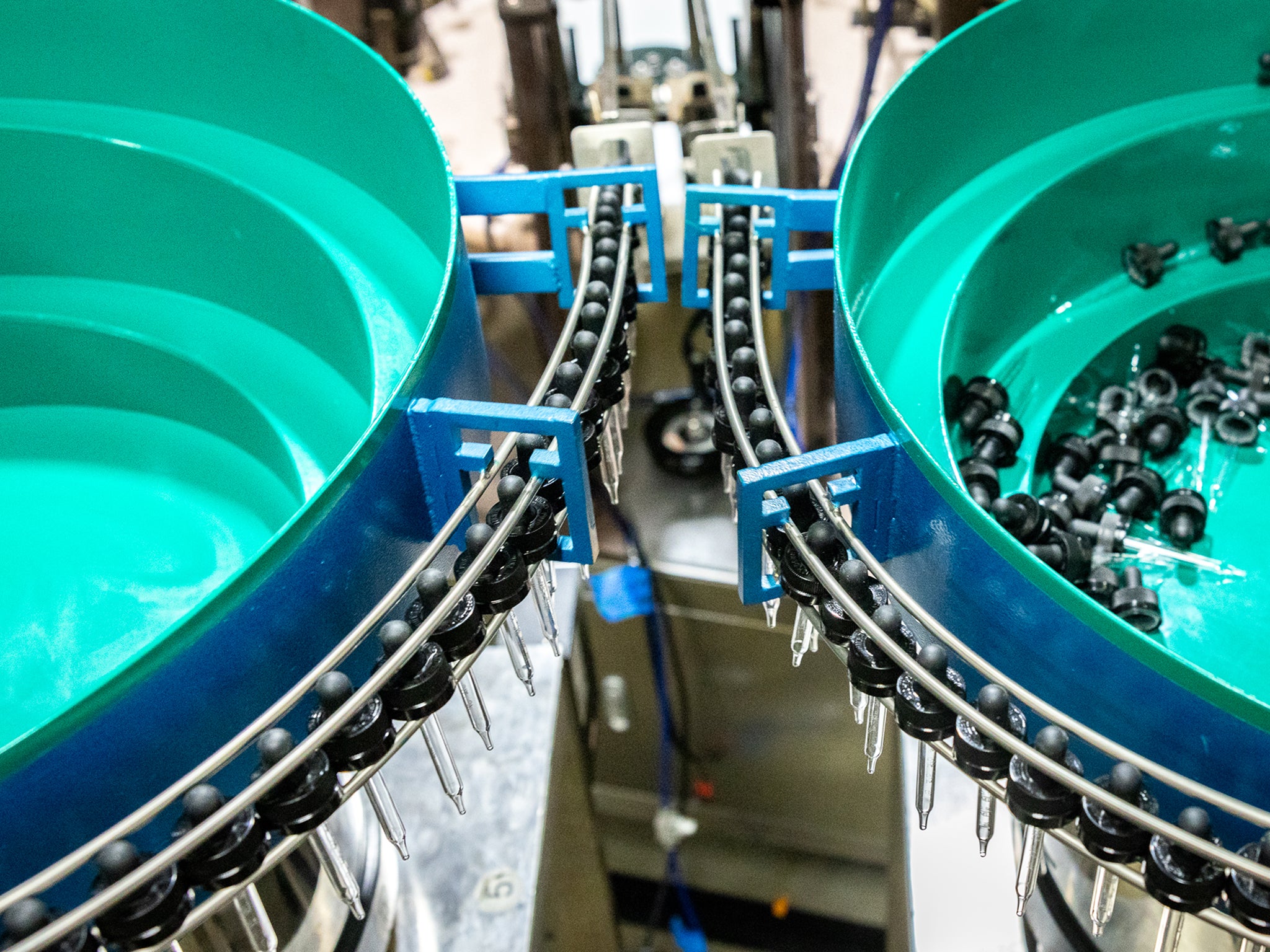 Two green circular vibrating feeders sorting and guiding small black plastic components along metal tracks in an industrial assembly line.
