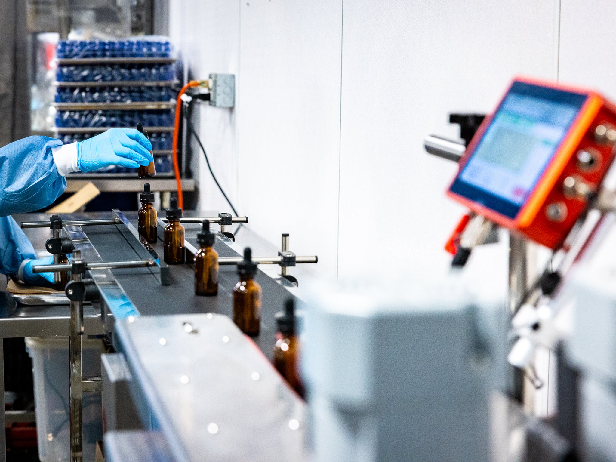 A worker in a lab coat manages machinery on an assembly line for tincture bottles.