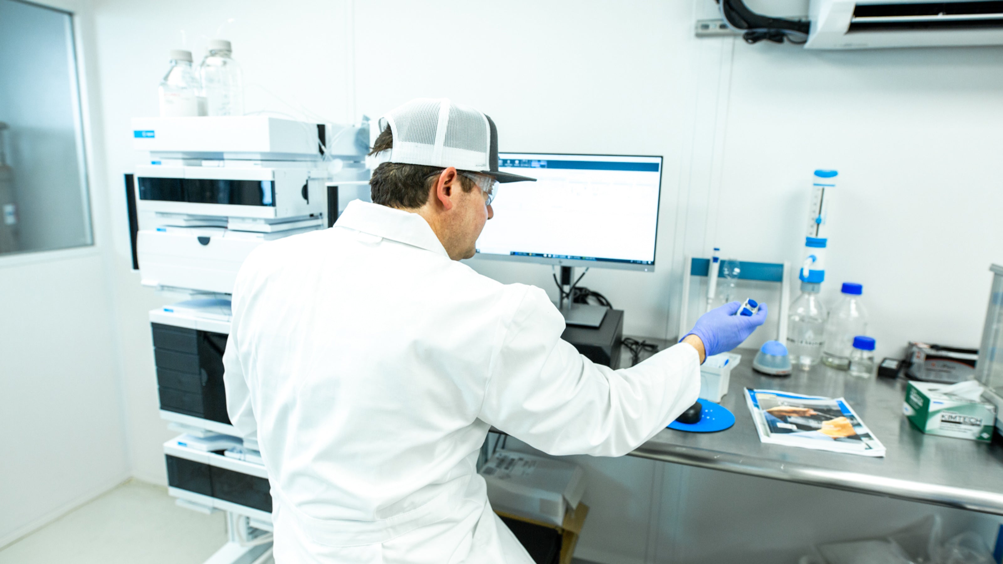Person in lab coat at a computer desk using a pipet